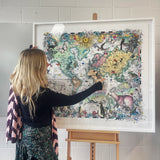 Woman looking at a colorful world map on an easel against a tiled wall.