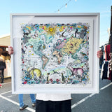 Framed world map with animal illustrations held by a person outdoors.